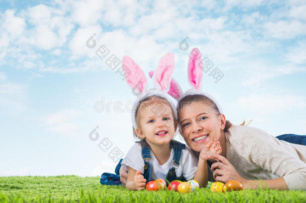 复活节兔子。 小女孩和妈妈穿着复活节兔子躺在草地上