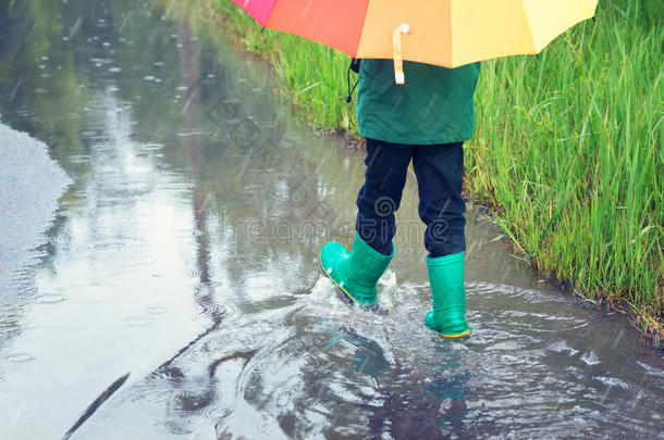 下雨天穿着雨鞋在水坑里散步的孩子