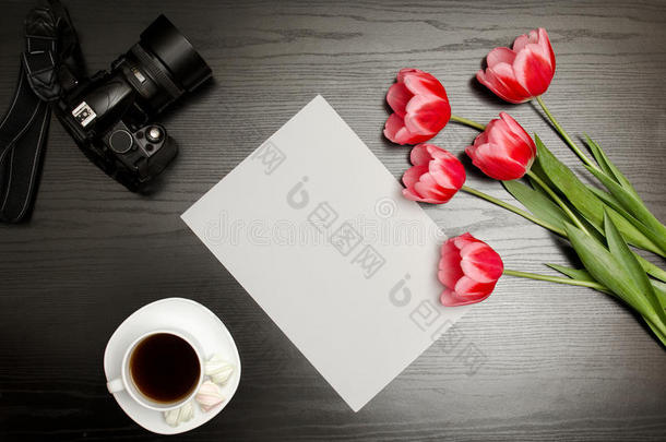 一张干净的纸，粉红色的郁金香，一个相机和一杯咖啡。黑桌子。俯视图