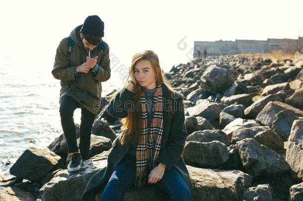 一对美丽而时尚的夫妇在岩石沙滩上散步。一对夫妇穿着夹克、帽子和靴子