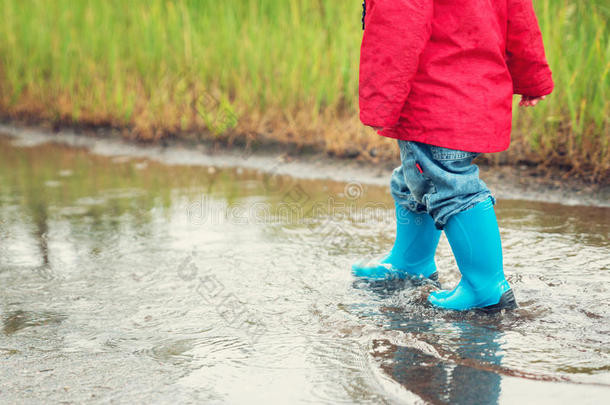 下雨天穿着雨鞋在水坑里散步的孩子
