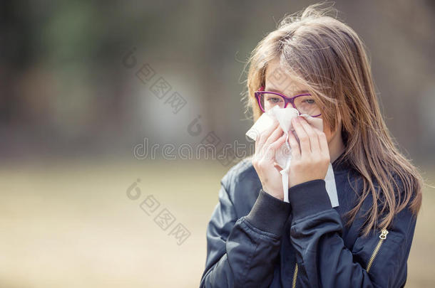 有过敏症状的女孩吹鼻子。 在公园里用<strong>纸巾</strong>的少女
