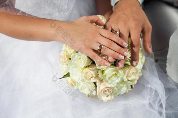 新娘和新郎双手捧着金色的<strong>结婚戒</strong>指，上面有白色玫瑰、奶油花的婚礼花束。