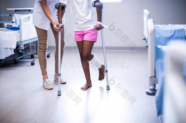 女医生协助女孩在病房用拐杖走路