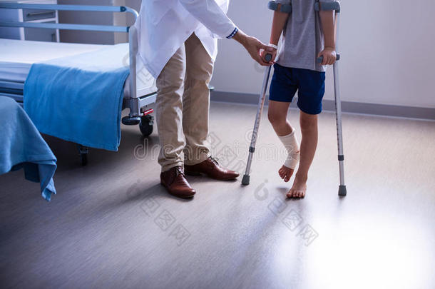 医生帮助受伤的男孩用拐杖走路