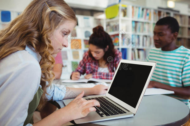 专注的女学生在学习背景下与同学一起使用笔记本电脑