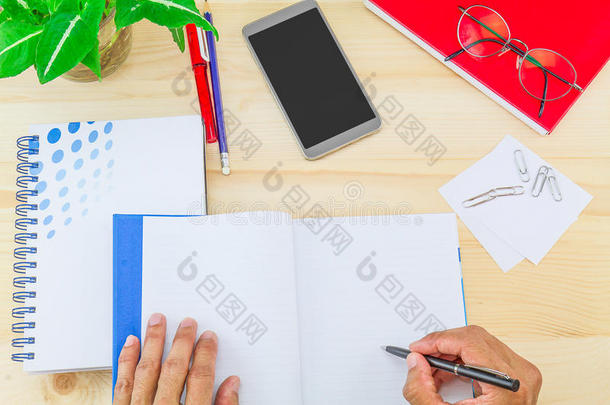 用办公用品、智能手机、眼镜和绿叶壶在木桌上的笔记本上手写