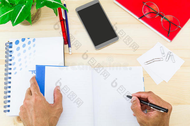 用办公用品、智能手机、眼镜和绿叶壶在木桌上的笔记本上手写
