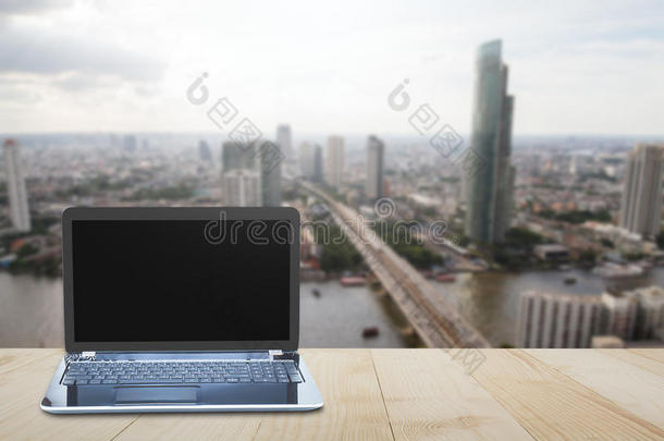 电脑笔记本电脑在木制<strong>桌面上</strong>模糊的城市背景