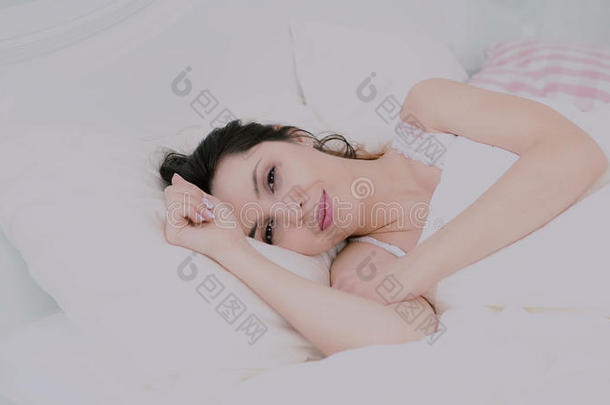 漂亮的年轻女子在家里的床上醒来。女孩看着镜头和可爱的微笑。清爽快乐的女人。