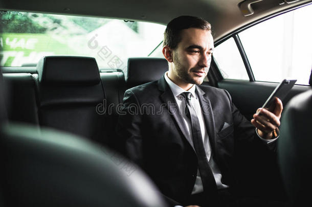 自信的年轻商人设置他的智能手机，看着相机，而坐在车里