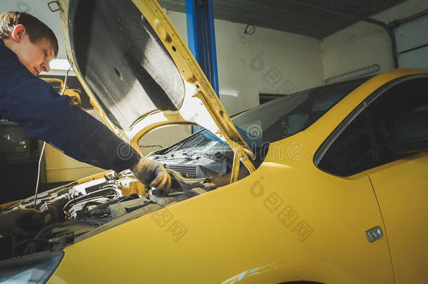 一名工人机械师检查黄色汽车、车库车间引擎盖上的电气
