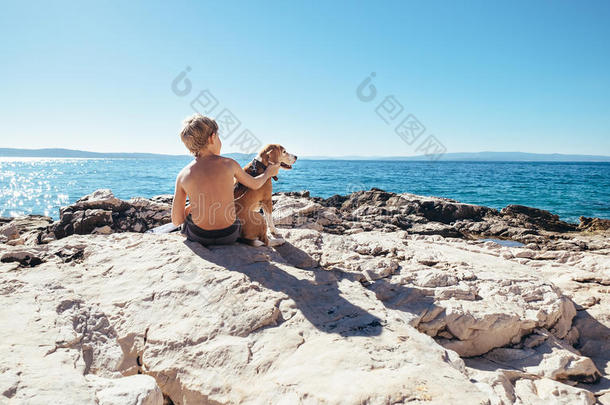 男孩和比格犬一起坐在岩石海岸阳光明媚