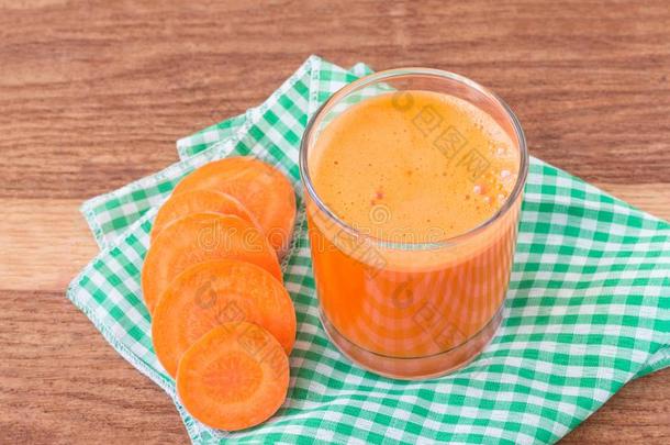 新鲜胡萝卜汁在玻璃和切片胡萝卜蔬菜在餐巾上的木制桌子。