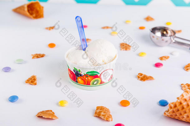 在白色背景的纸杯中关闭香草冰淇淋，里面有彩色糖果、华夫饼、冰淇淋勺子