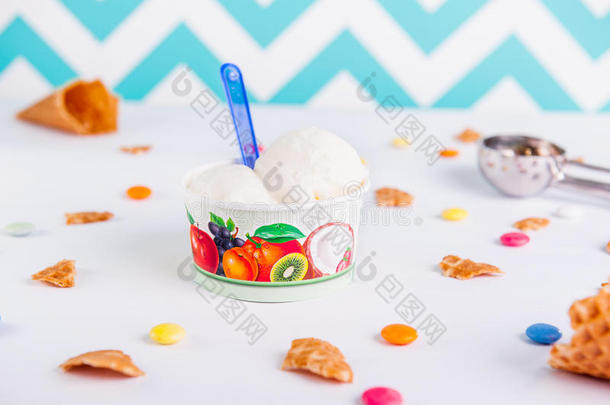 在白色背景的纸杯中关闭香草冰淇淋，里面有彩色糖果、华夫饼、冰淇淋勺子