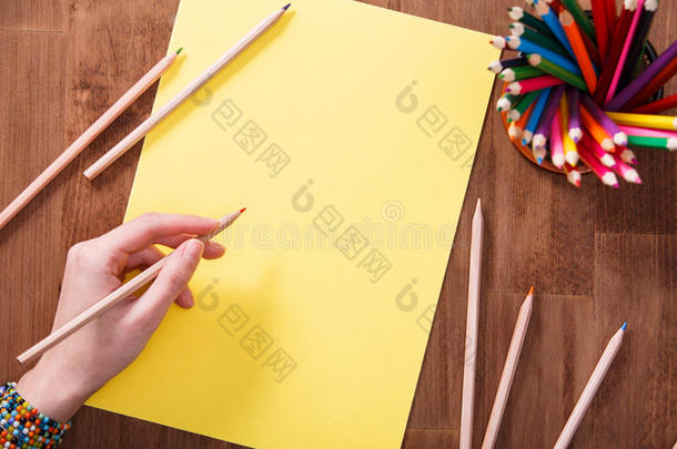 女孩手绘，空白黄纸和彩色铅笔在木桌上