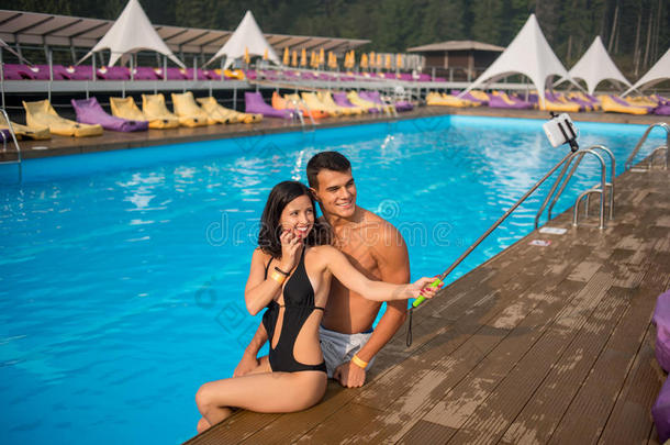 男人和女孩在游泳池边摆姿势，有完美的水，并在度假村与Monopod合影