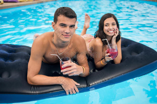 特写男人和一个微笑的女人躺在游泳池里的床垫上，喝着鸡尾酒享受假期。 专注于那个人