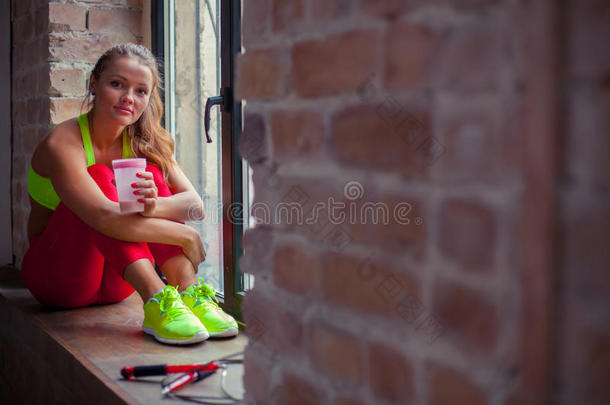 美丽的年轻女孩坐在窗台上喝酒。