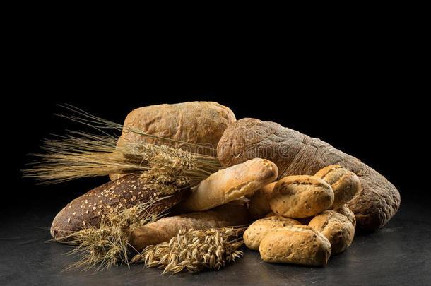 黑木桌子上的面包、面包、面包和面包。 黑巴上的黑麦、大麦、小麦、燕麦和许多新鲜混合面包