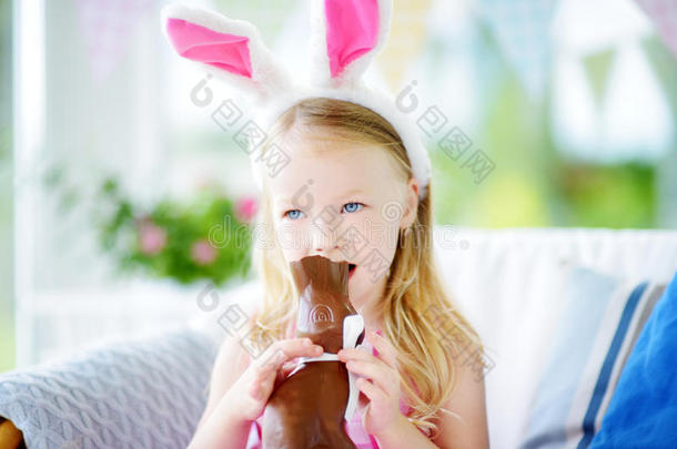 可爱的小女孩戴着兔子耳朵吃巧克力复活节兔子