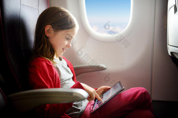 可爱的小女孩乘飞机旅行。 孩子坐在飞机窗口边，用数字平板电脑