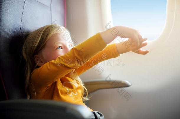 坐飞机旅行的可爱的小女孩。坐在飞机窗口向外看的孩子。