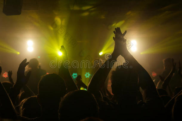球迷们在夜总会的摇滚音乐会上挥舞着他们的手，在美丽的金色灯光下