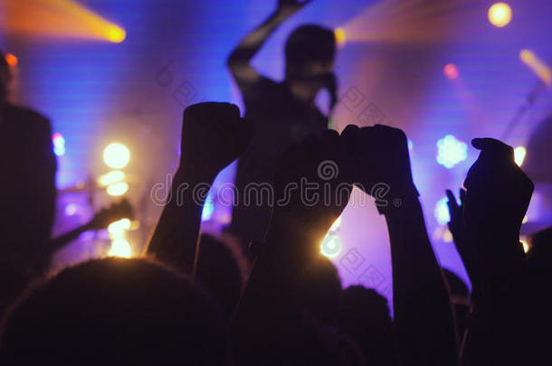 球迷们在夜总会的摇滚音乐会上挥舞着他们的手，在紫色的美丽的金色灯光下