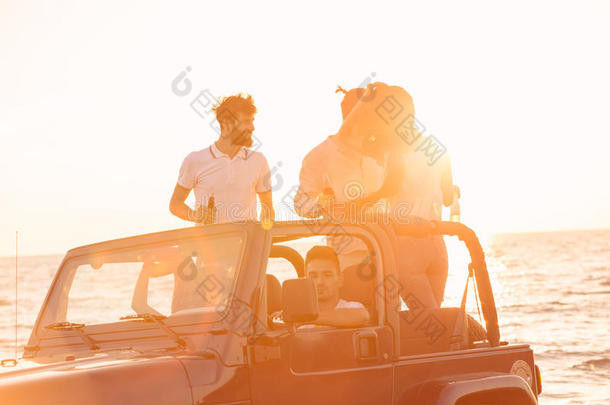 五个年轻人在日落时在海滩上开敞篷车玩得很开心。