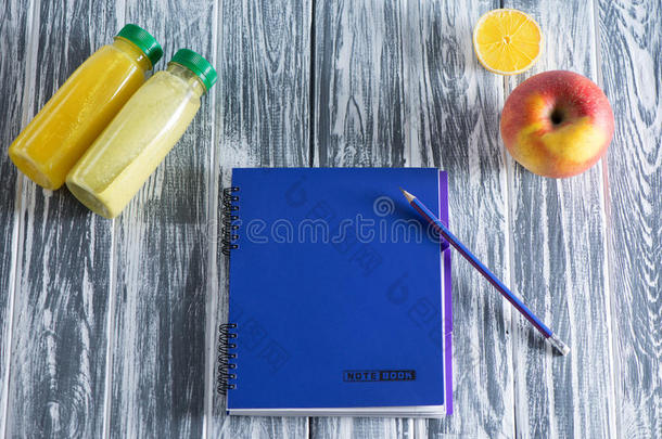 一本笔记本，上面有铅笔、苹果、果汁和半个柠檬，放在一张木制的光桌上。 顶部有免费的铭文空间