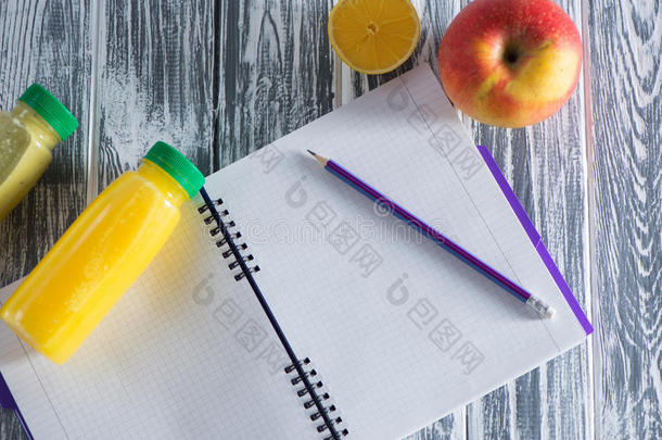 一本笔记本，上面有铅笔、苹果、果汁和半个柠檬，放在一张木制的光桌上。 一个铭文的自由空间