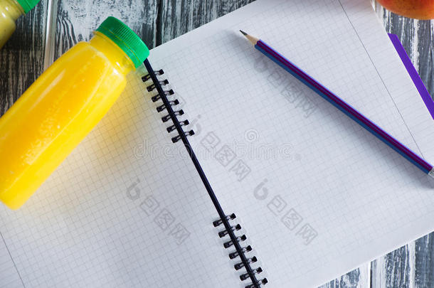 一本笔记本，上面有一支铅笔和一瓶果汁，贴在一张木制的光桌上。 笔记本上铭文的自由空间。 顶部a
