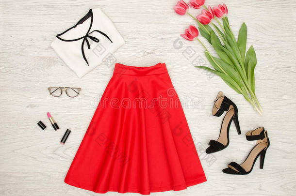 时尚概念。 红色裙子，衬衫，太阳镜，口红，黑色鞋子和粉红色郁金香。 顶部视图，轻木背景