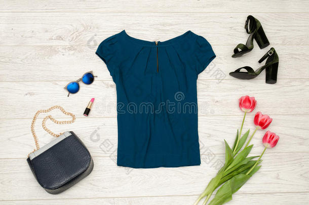 时尚概念。 蓝色衬衫，手提包，圆形眼镜，口红，黑色鞋子和粉红色郁金香。 顶部视图，轻木背景