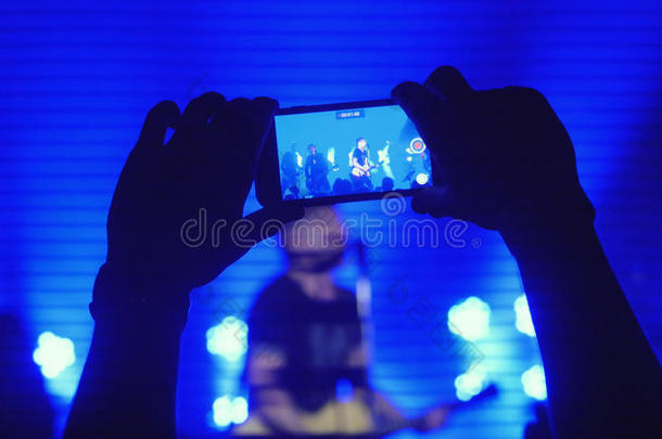 歌迷们用智能手机在摇滚音乐会上用美丽的蓝色背景录制视频
