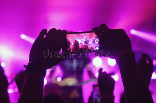粉丝们女人的手用智能手机在摇滚音乐会上用粉红色录制视频
