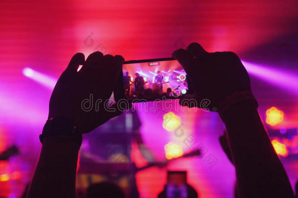 粉丝女人的手在摇滚音乐会上用智能手机录制红色背景颜色的视频