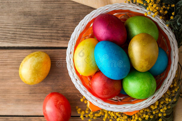 五颜六色的复活节彩蛋在篮子和含羞草花在乡村木桌上。