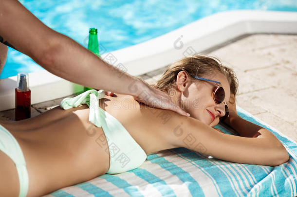 帅哥在游泳池附近的女孩身上涂防晒霜。