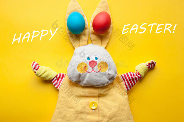 复活节装饰从一个手工玩具兔子和彩色鸡蛋在橙色的背景。 用快乐复活节这个词