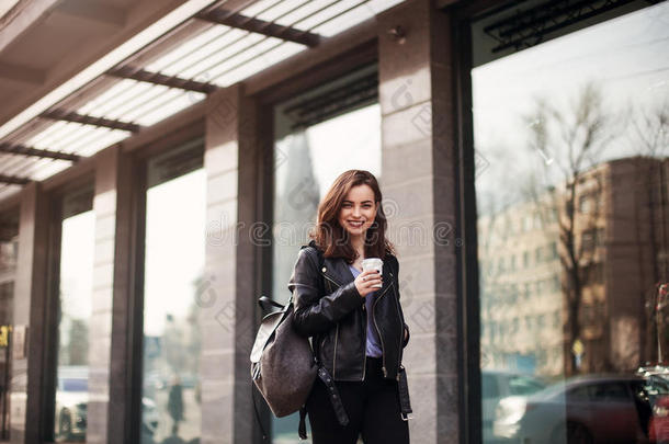 一个穿着休闲装的漂亮女孩在城市里散步的时尚街头风格的特写。漂亮的黑发女人喝咖啡。