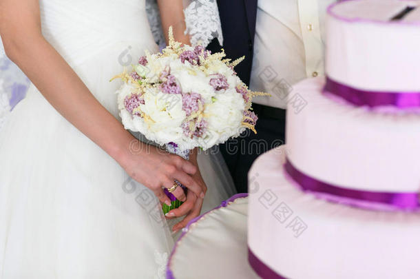 新娘站在婚礼蛋糕后面，手里拿着一束花