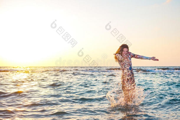 美丽的女孩穿着五颜六色的衣服，在夕阳在海洋中溅起水花