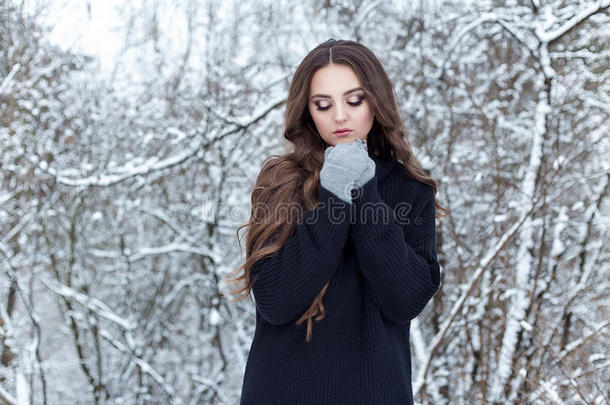 美丽的年轻女人，留着长长的黑发，穿着黑色夹克和手套，在冬天的树林里孤独地散步