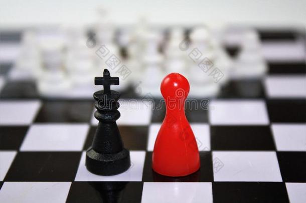黑色<strong>国王</strong>和<strong>红色</strong>女王雕像的卢多和白色模糊的棋子在远处。 在棋盘上有趣的概念。