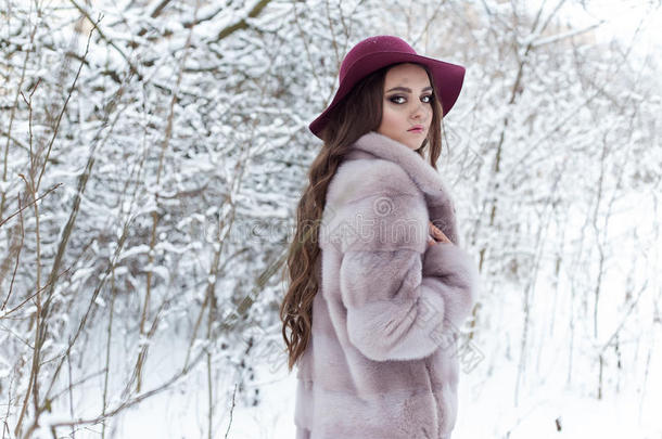 美丽可爱优雅的女孩穿着毛皮大衣和帽子，在冬天的森林里散步，明亮的霜冻的早晨