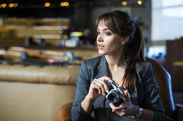 美丽的女孩摄影师手里拿着相机。 年轻的女人看着取景器，在咖啡馆里拍照。