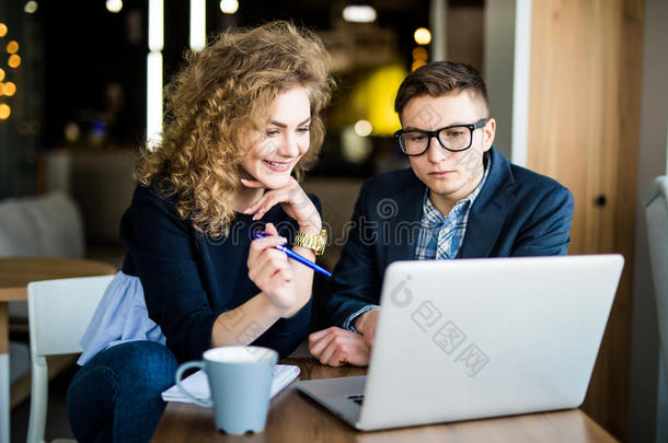 两个同事在笔记本电脑上工作，在现代办公室讨论。 快乐的女人在笔记本电脑屏幕上看书